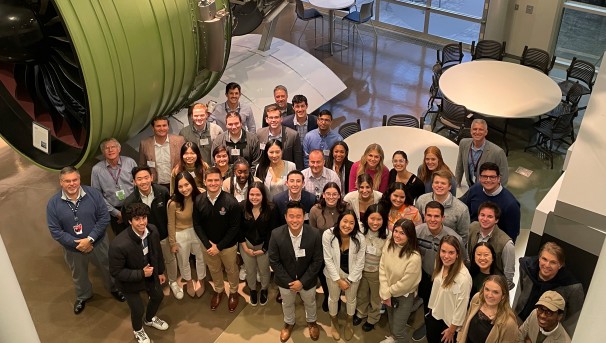 Group of students, faculty and staff standing in a room looking up smiling at the camera