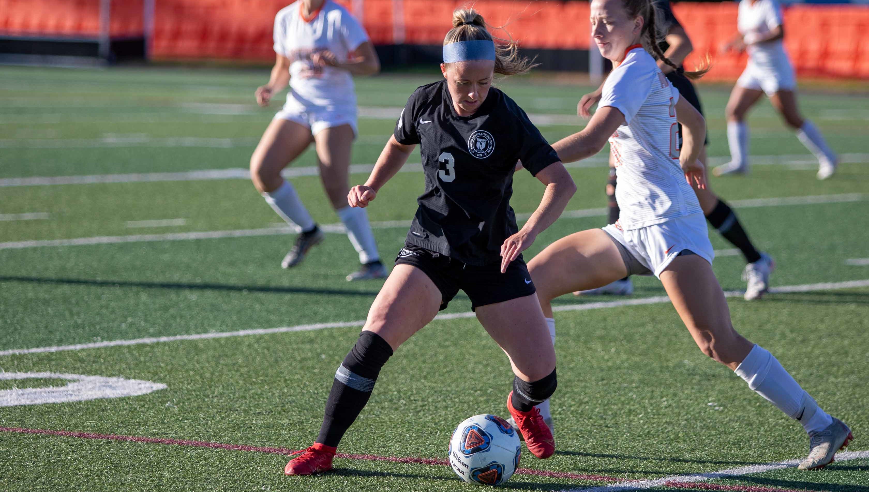 A women's soccer player on the field with the ball.