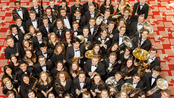 The Symphonic band stands on a buckeye carpet, holding their instruments.