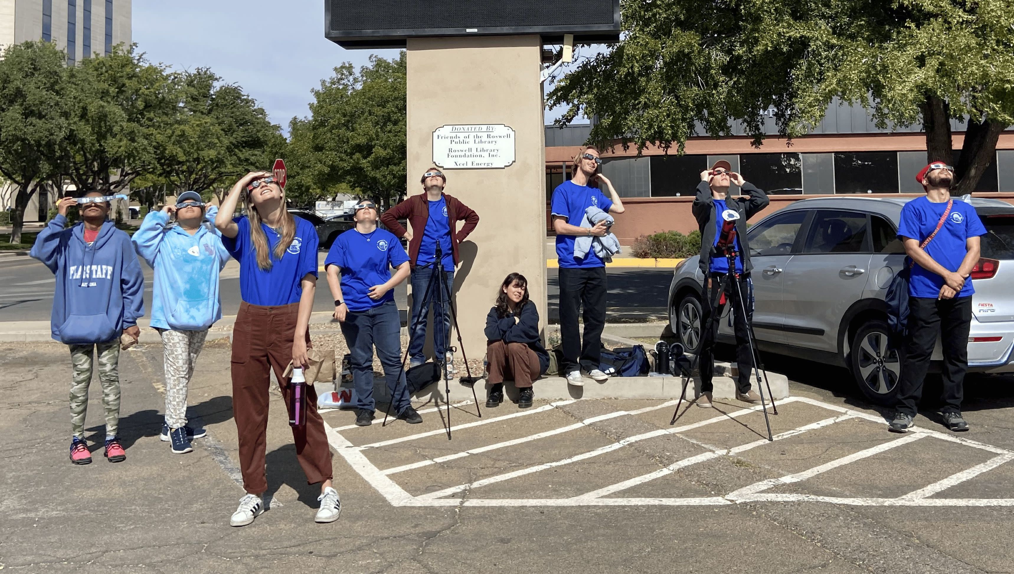 The club is posing under the famous “Welcome to Roswell” sign featuring a UFO design.