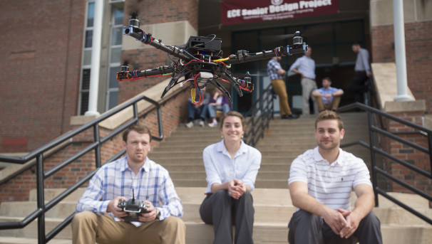 Students sitting on the steps of the Engineering building flying a drone