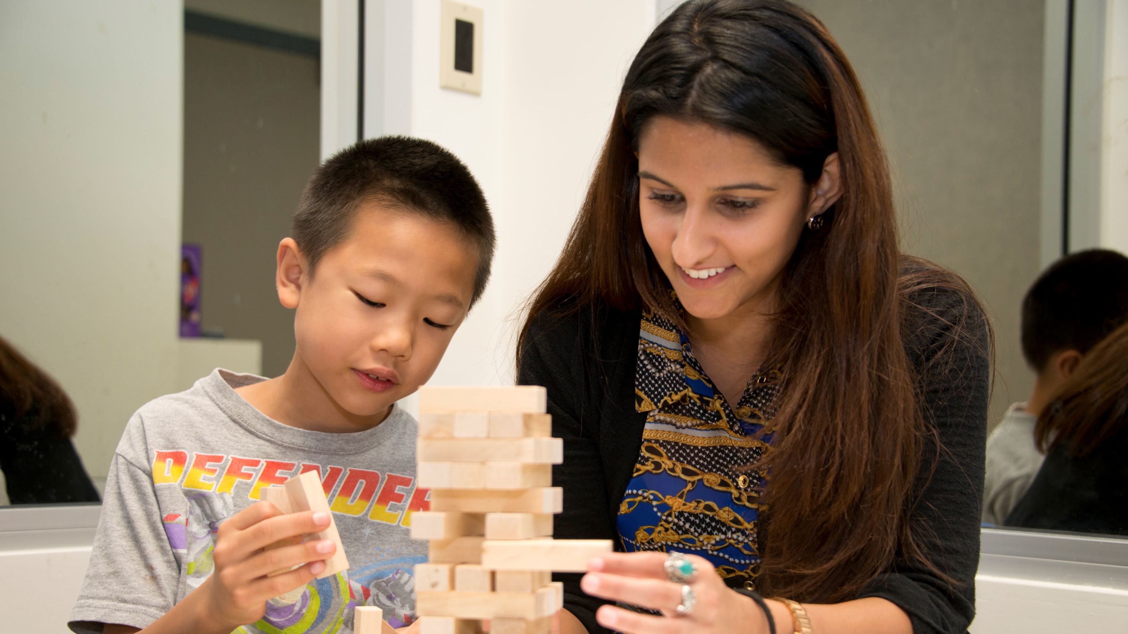 Education student works with a young child using wooden blocks in a learning activity.
