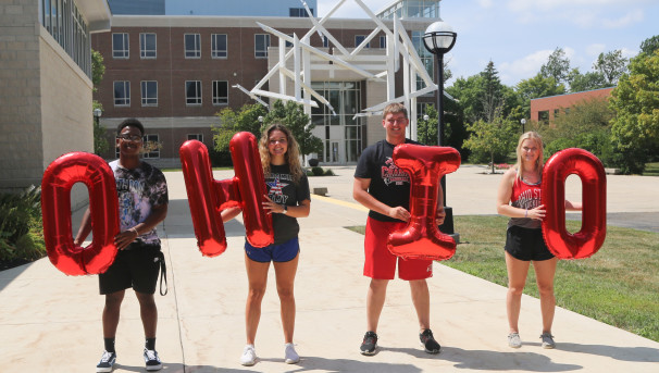 Lima students with a brick campus building behind them, all holding red balloons that spell out OHIO