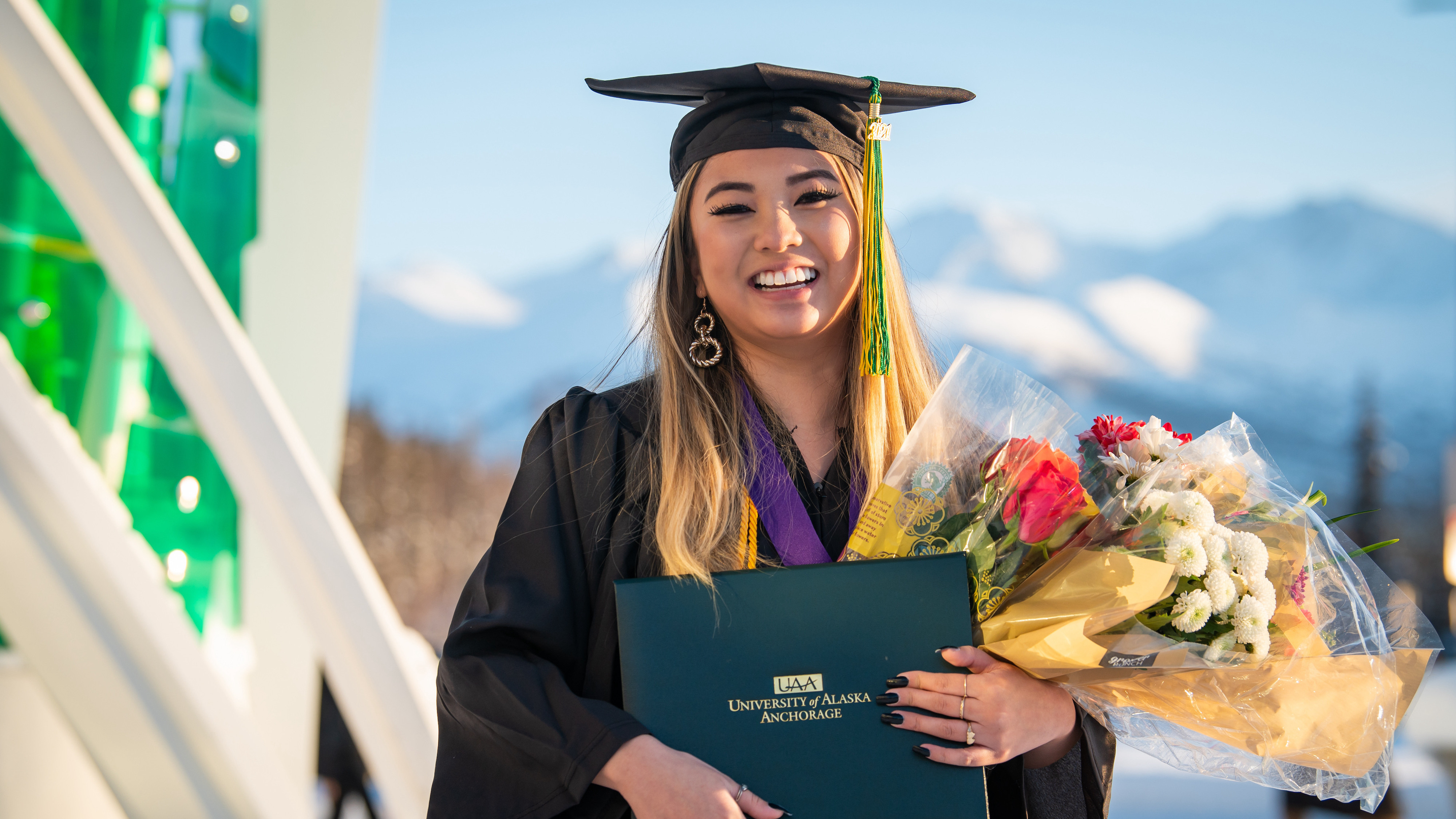 UAA Student, holding degree, mountain background