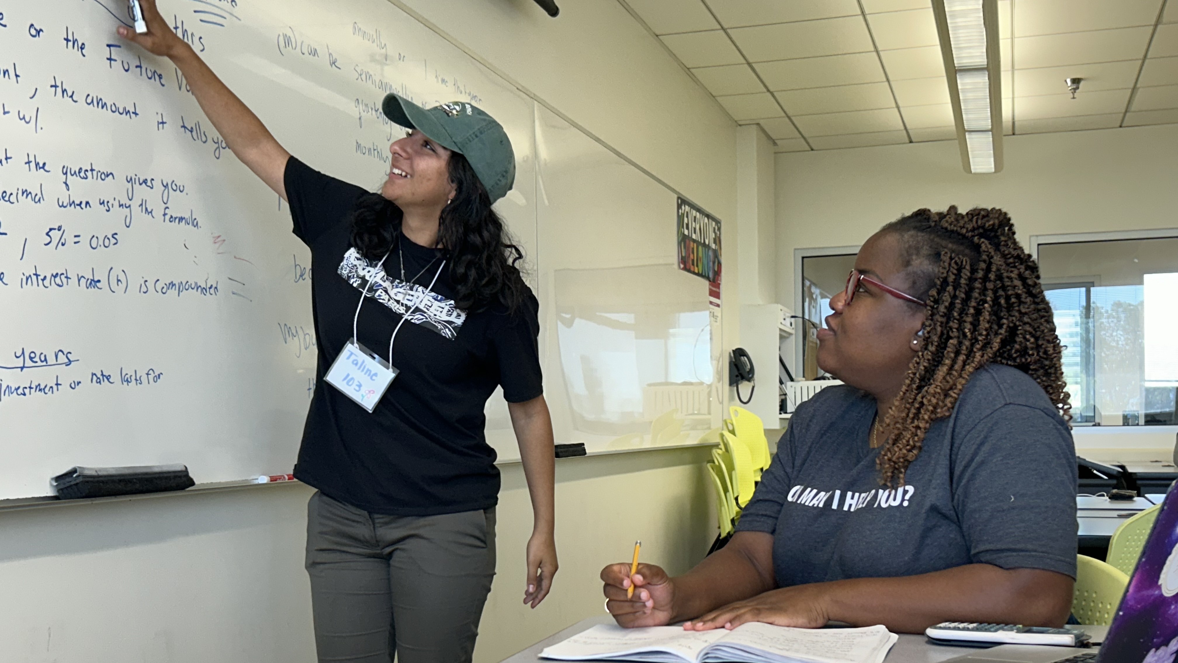 Mentor teaching a student in a classroom, pointing to whiteboard with instructions.
