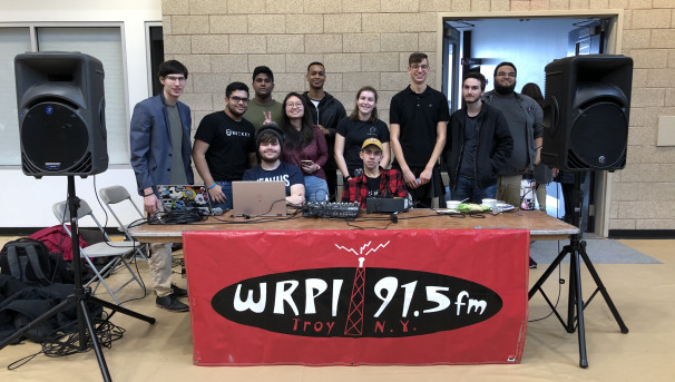 Students behind a table with portable broadcasting equipment and a WRPI banner