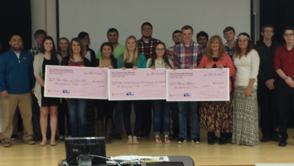 A group holding three, pick Pay It Forward checks at the front of a classroom
