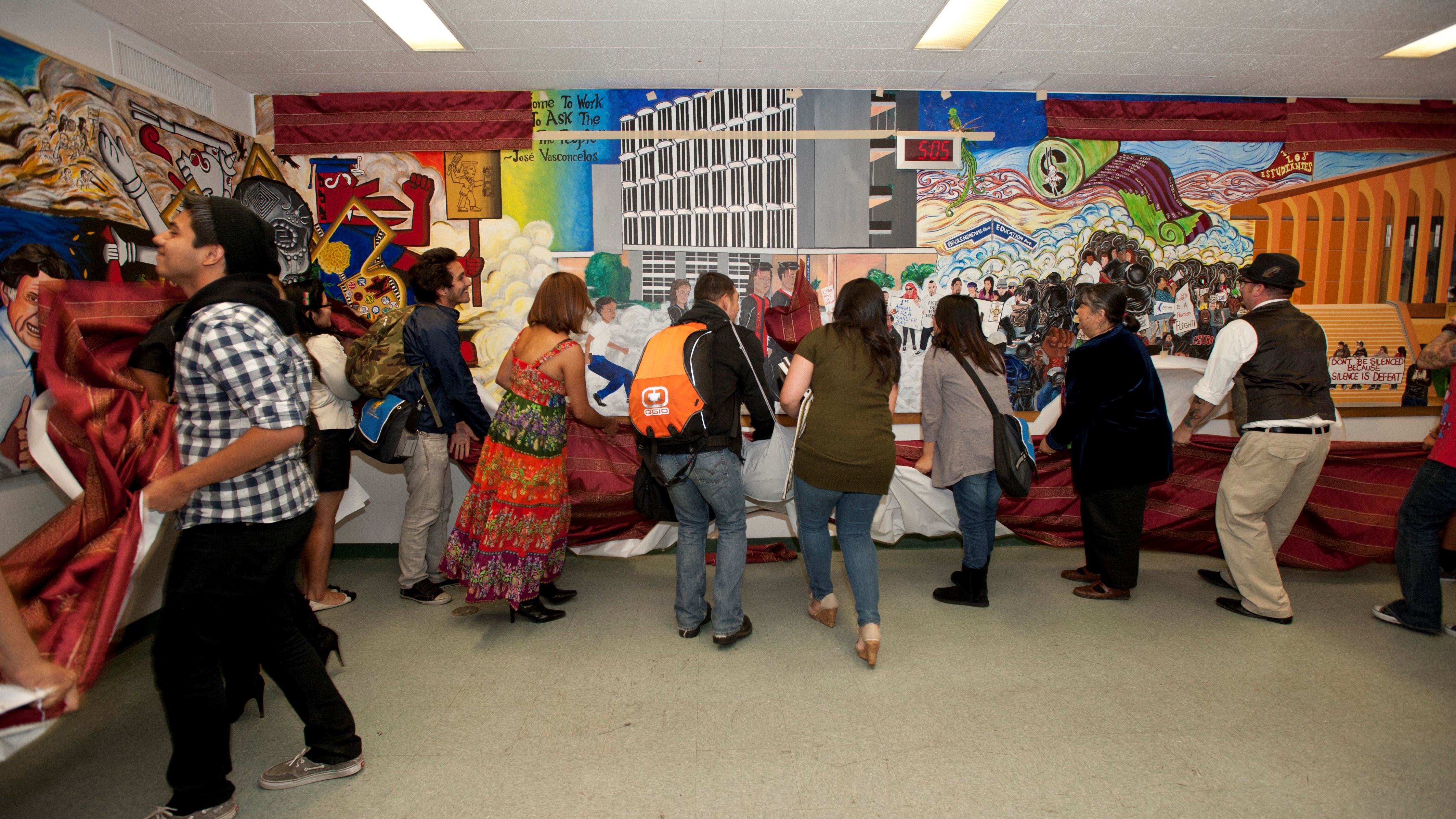 Students unveil a colorful mural celebrating Chicana/o heritage and activism inside a campus hall.