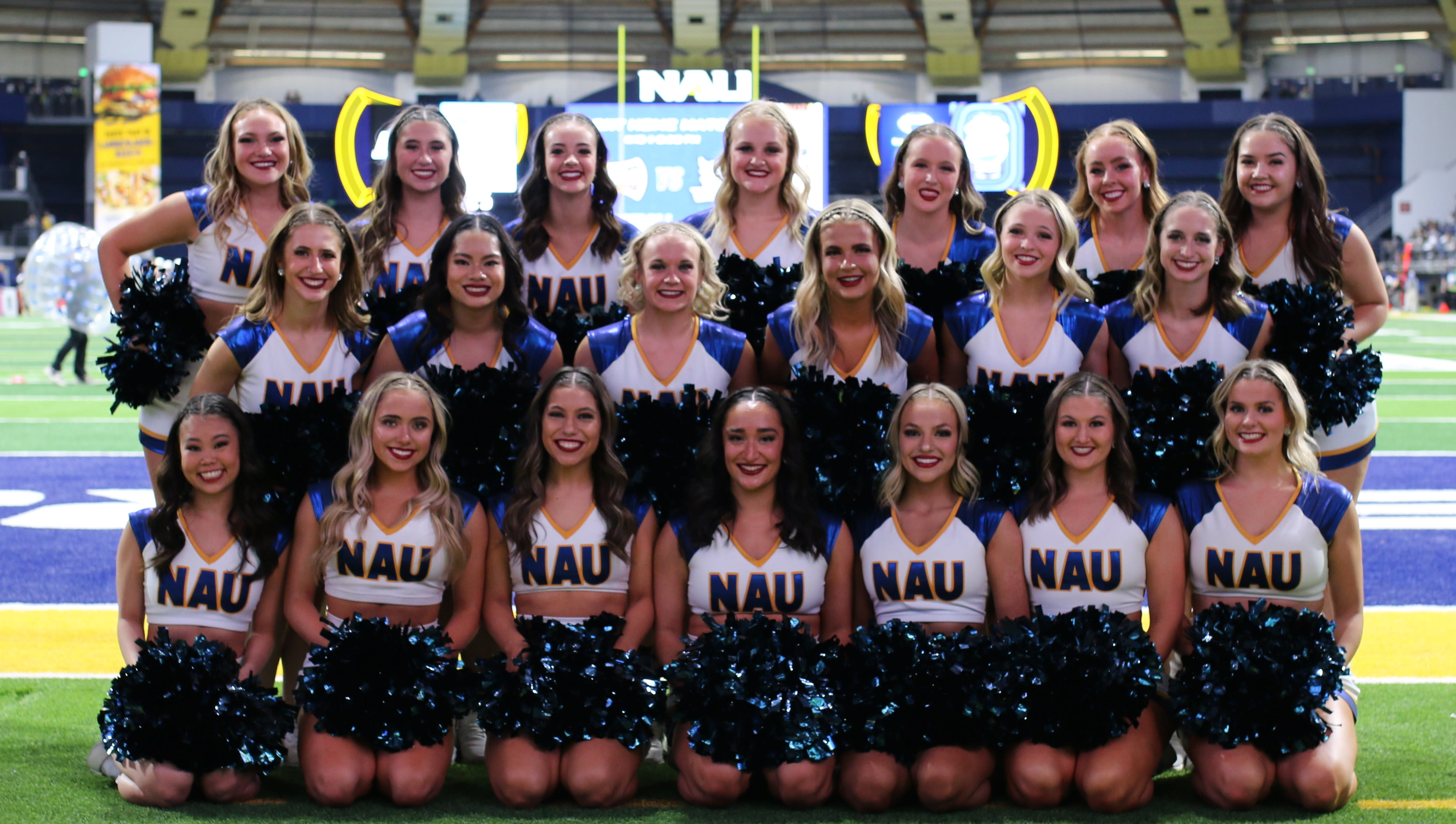 Dance Team posing on field with white uniform and blue pom-poms