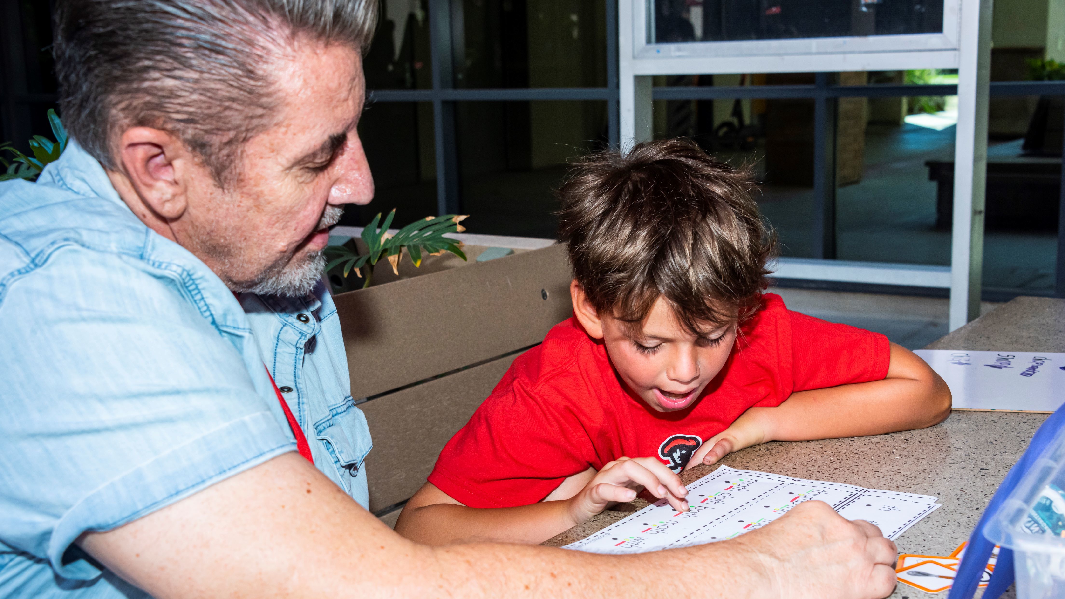 A man helping a young boy with reading a sheet of words