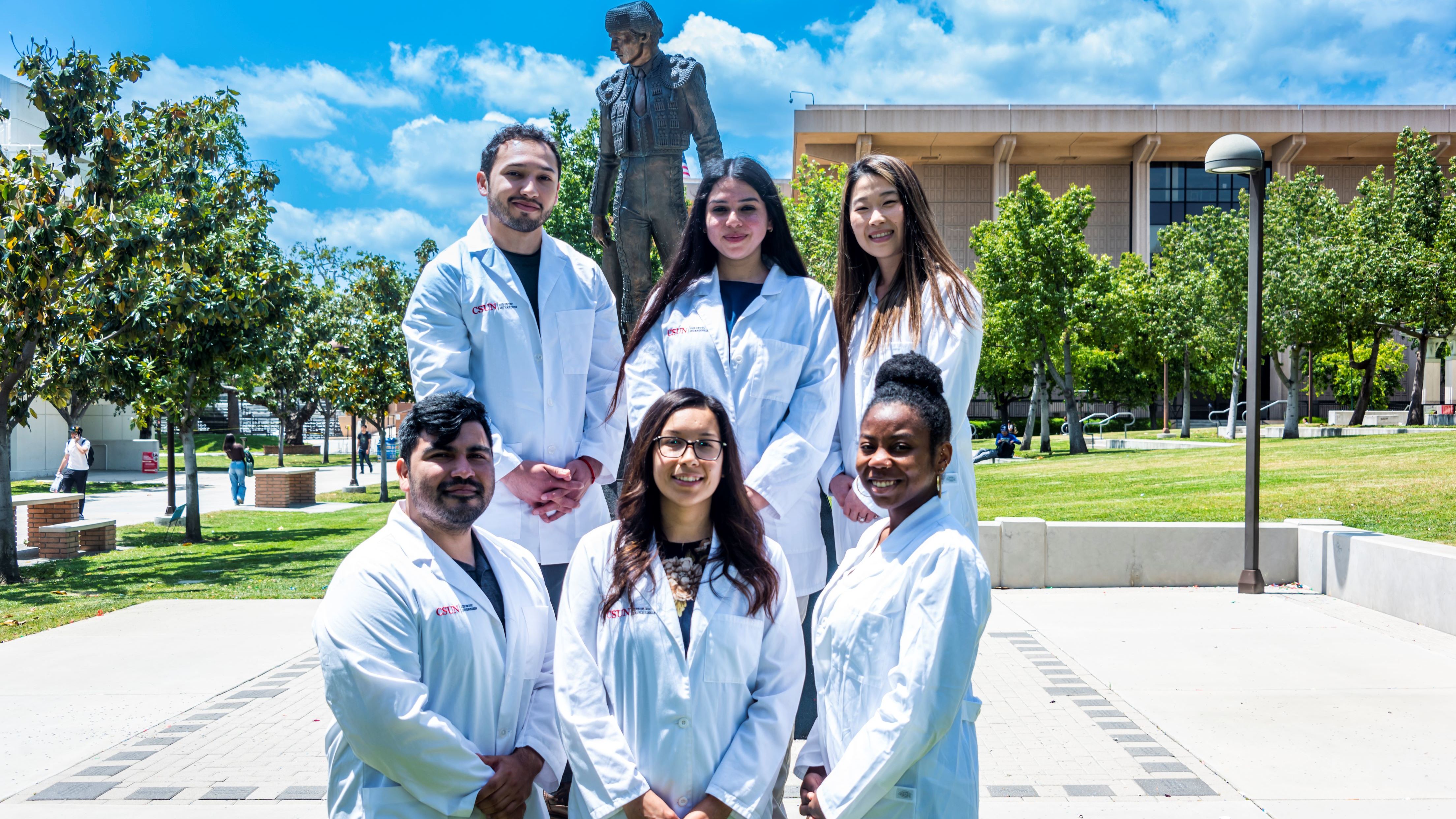 CSUN Health and Human Development students in white lab coats pose outdoors on campus.