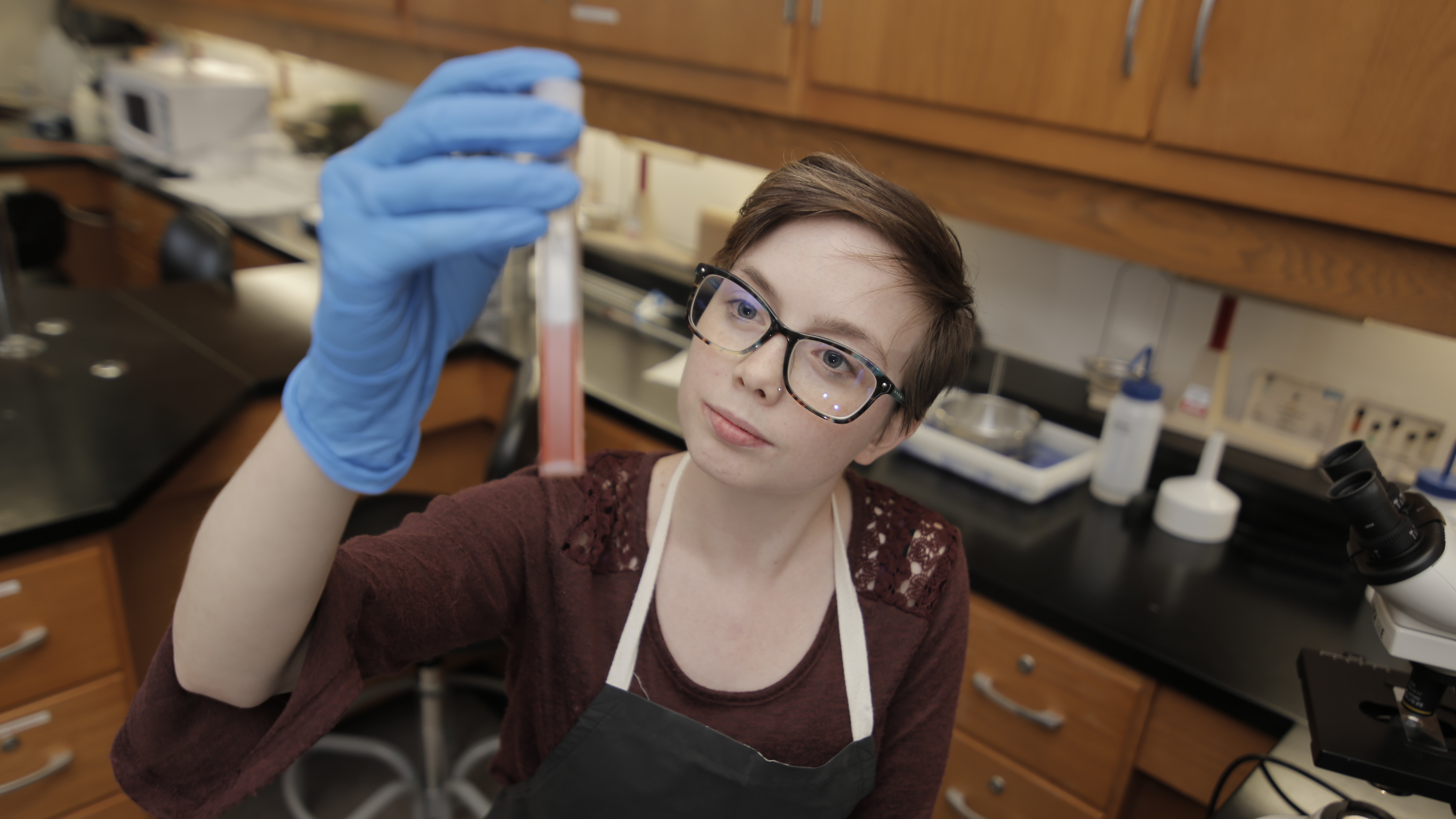 A student in a lab holds up a vial to the light.