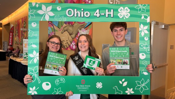 Three 4-H youth standing in middle of large photo frame holding project book guides.