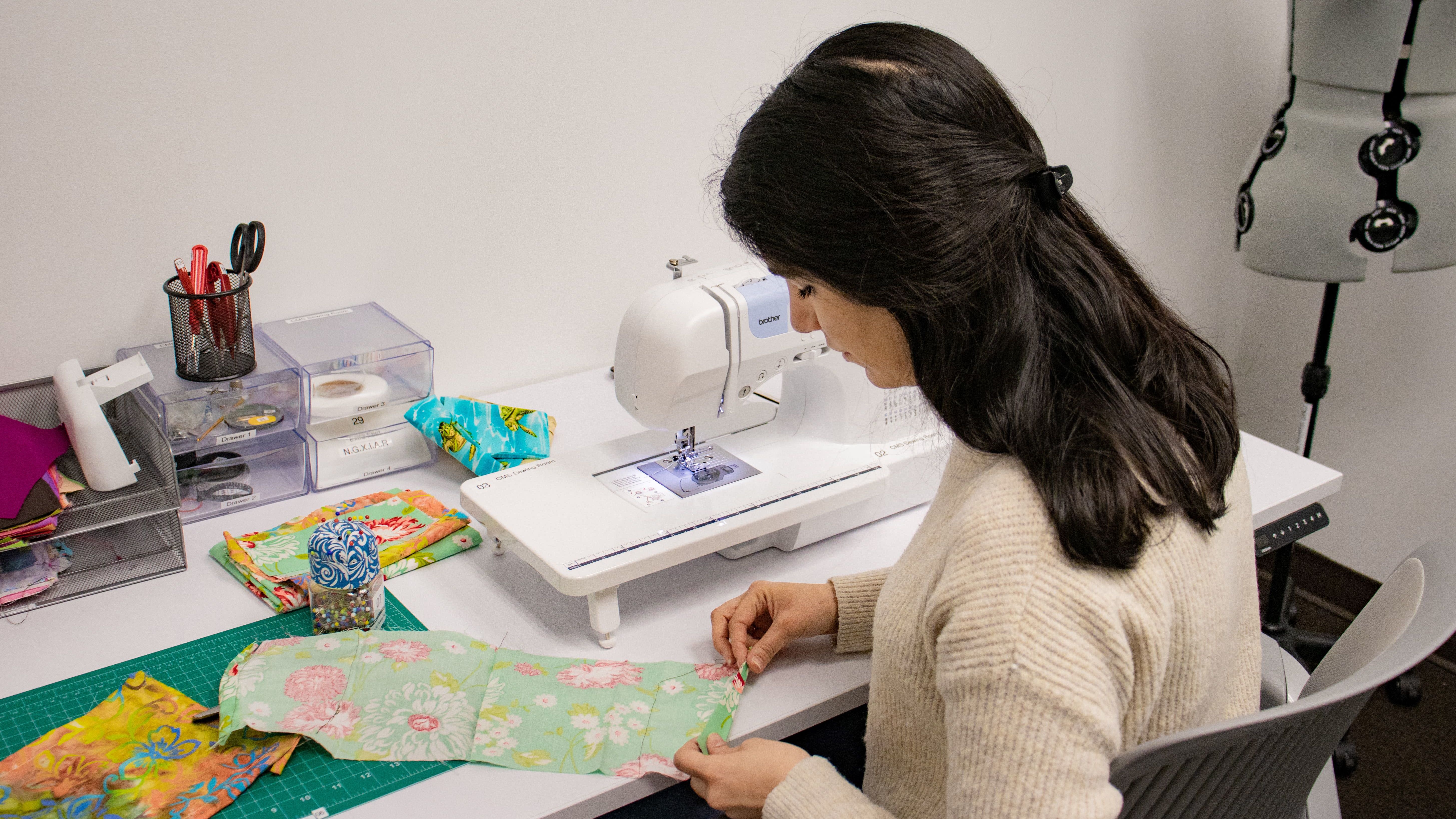 Student sews floral fabric in hands-on textile design space at Maker Studio.