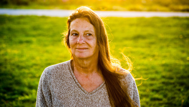 Laurie standing in a green field. The sun is shining on her back as she looks past the camera