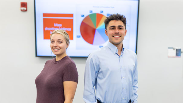 Students standing back to back in front of a screen displaying their presentation with a pie chart