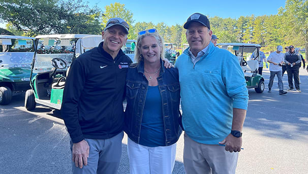 Three individuals standing in front of golf carts at a golf outing for ovarian cancer research