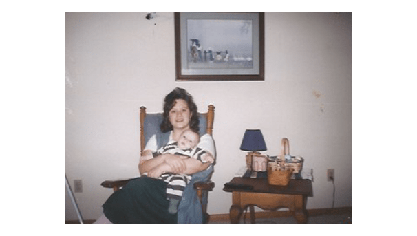 A woman sitting in a blue cushioned rocking chair holds a baby