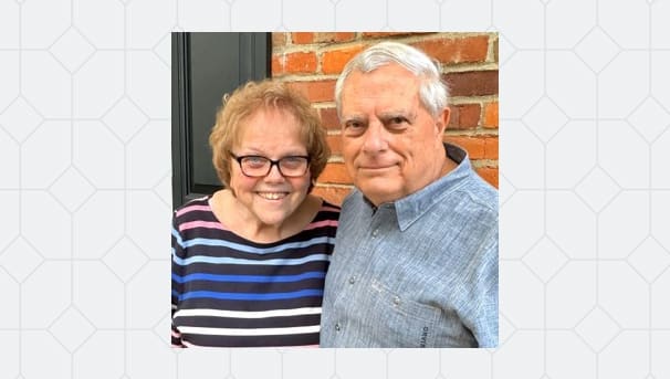 Barbie and Jim Tootle standing next to each other while smiling. They stand before a brick wall