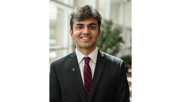 Tanish Gandhi's professional headshot. He wears a black blazer and a red and navy blue tie