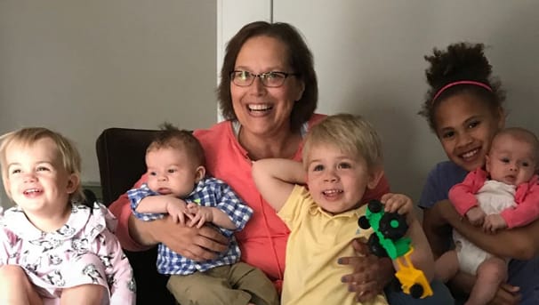 A woman and five children of various ages sitting on a large chair, smiling towards the camera