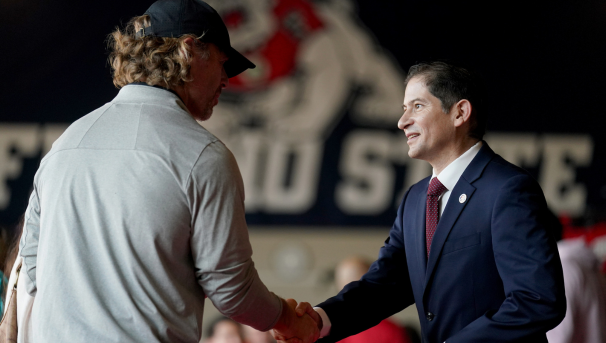 President Saul shaking hands with another coach, fresno state logo with four-paw bulldog in back