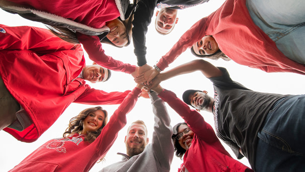 Smiling students in a circle with hands in the middle