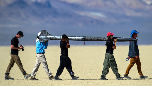 Students standing in a field while holding their model rockets.