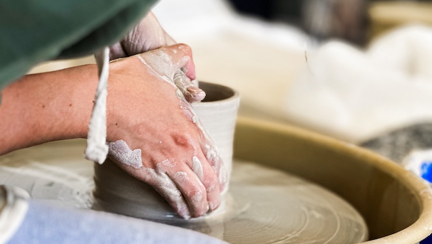Hands at a pottery wheel making a cylindrical vessel