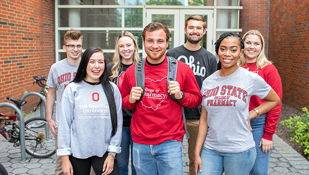 Seven pharmaceutical students wearing OSU gear in front of a classroom building