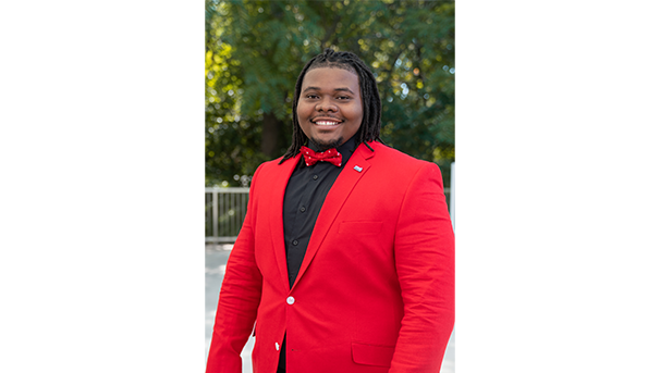 Sly Worthy Jr.'s professional headshot. He wears a red suit, black button up, and a red bowtie