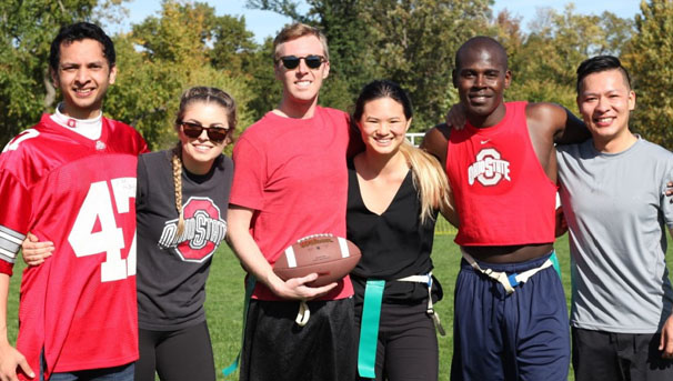 Group of 6 students playing flag football stand together holding a football for a photo