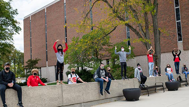 Galvin Hall Basement Club posed outside. Four students do O-H-I-O with their arms