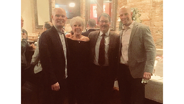 Four individuals dressed in formal attire, huddled together for a photo