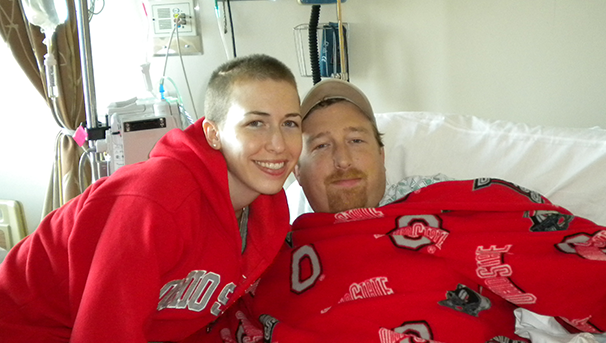 Two individuals smiling wearing Ohio State gear while next to each other in a hospital bed