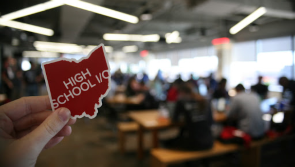 High School I/O student hackathon sticker logo. Behind it is a blurred image of individuals working