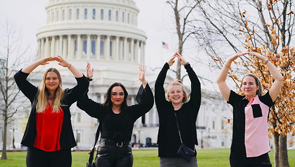 Four individuals standing outside holding up their arms for O-H-I-O