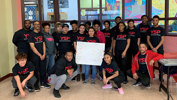 Group of students and teachers posing for a photo and holding a sign