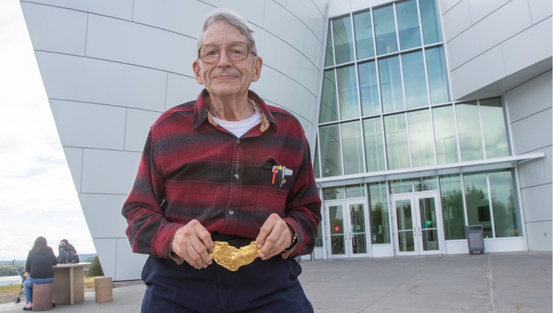 Roger Burggraf holds a gold nugget and stands in front of the museum building.