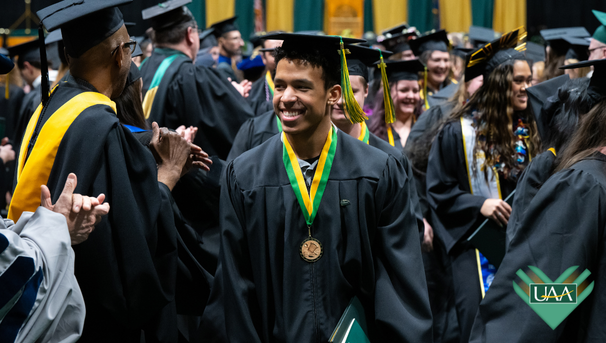 UAA graduate smiles while walking through cheering faculty and classmates at commencement