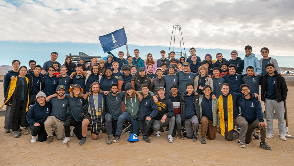 Group of excited college students posing for a picture before an important rocket launch.