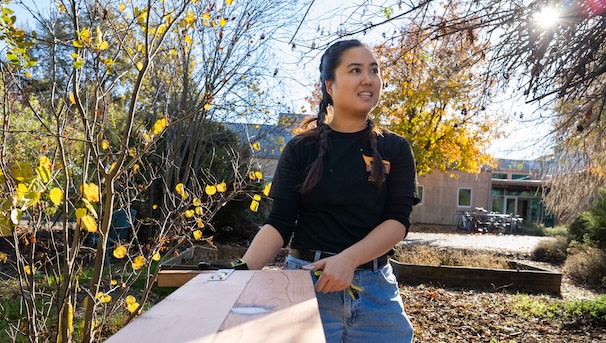 A UC Davis graduate student is outside on a farm and is holding a wooden board in their hands.