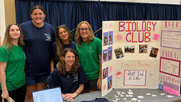 Five students smiling behind a Biology Club poster