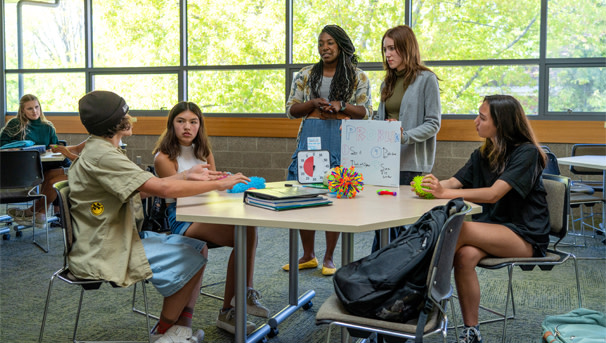 A female UO student and her supervisor speak to a seated female high school student in a classroom