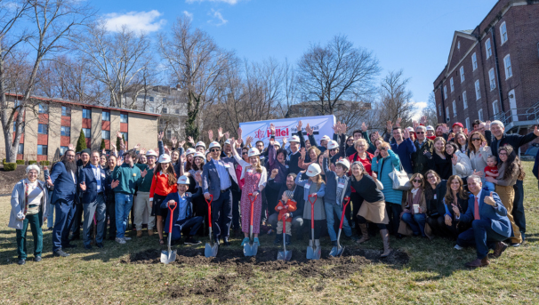 Image of a group of people crowded together for a photo. Six people in front holding shovels.