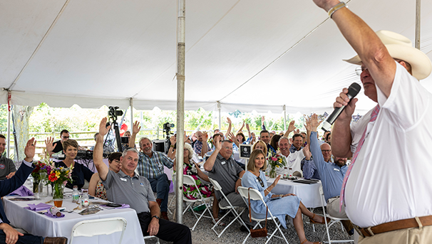 Individual standing up talking in a microphone to a crowd with their hands raised