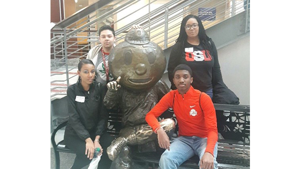 Four students in a photo with Brutus statue at the Ohio Union