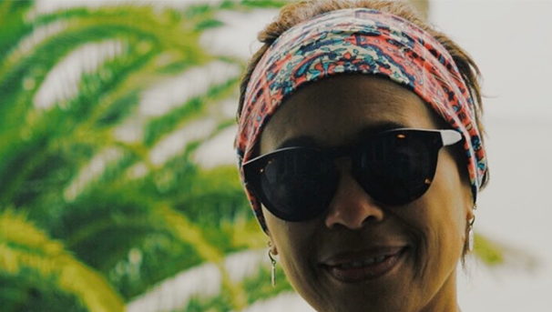 Individual wearing sunglasses and a colorful headband smiles for a picture while outside