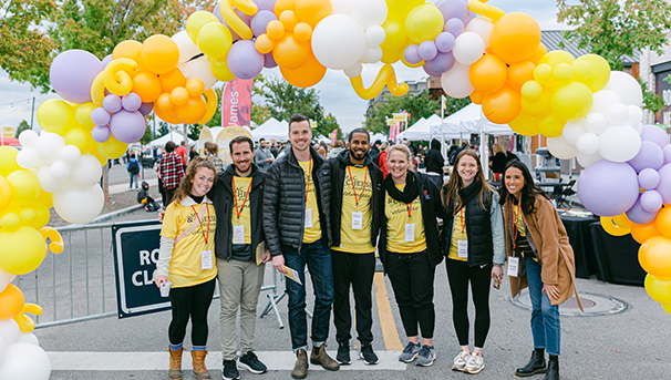 Group of volunteers standing outside under a balloon arch at The Columbus Mac & Cheese Festival