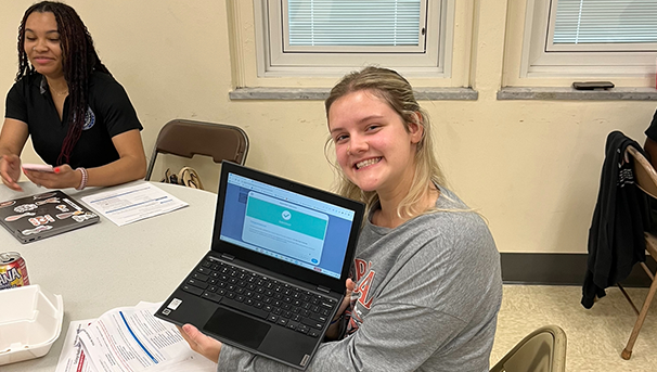 Student smiling at table holding laptop open